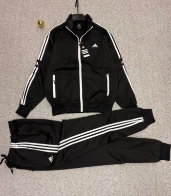 A stylish Adidas tracksuit laid out on a grey surface, consisting of a black jacket with white stripes and a matching pair of pants, ideal for athletic and casual wear.