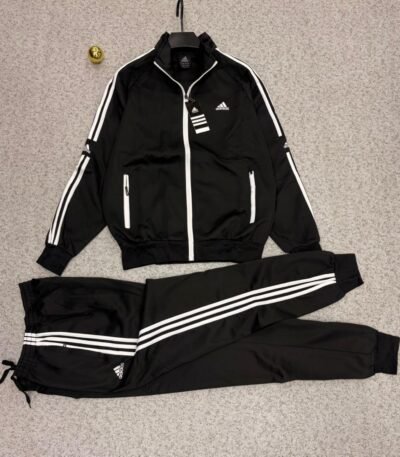 A stylish Adidas tracksuit laid out on a grey surface, consisting of a black jacket with white stripes and a matching pair of pants, ideal for athletic and casual wear.