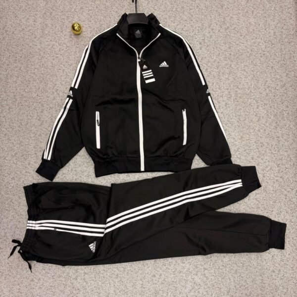 A stylish Adidas tracksuit laid out on a grey surface, consisting of a black jacket with white stripes and a matching pair of pants, ideal for athletic and casual wear.