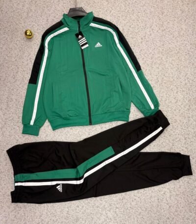 Adidas tracksuit laid out on a beige surface, featuring a green jacket with black and white stripes and matching black pants.