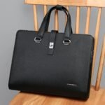 A luxurious black leather briefcase with silver accents, placed on a wooden chair, showcasing its sleek design and premium quality.