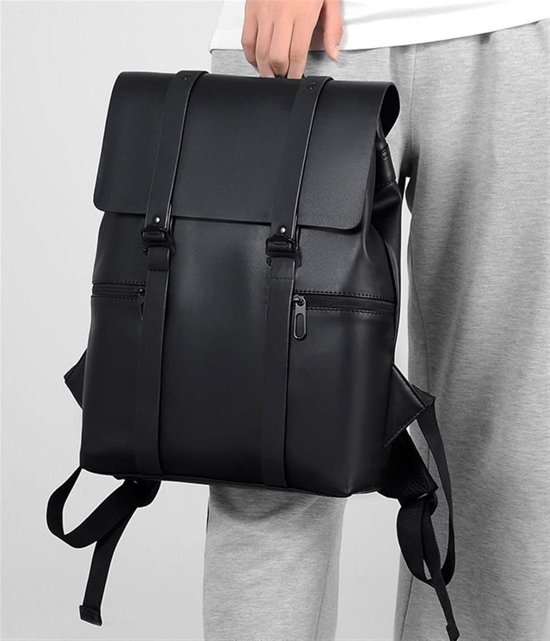 A stylish black leather backpack with flap closure and adjustable straps, carried by a man in casual attire.