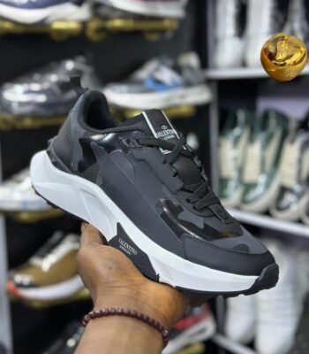 A close-up shot of a hand holding a black Valentino Garavani sneaker, showcasing its sleek design and luxurious details.