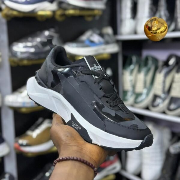 A close-up shot of a hand holding a black Valentino Garavani sneaker, showcasing its sleek design and luxurious details.