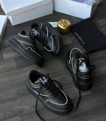 A pair of black leather Givenchy sneakers with white accents, displayed on a wooden floor with their box and packaging.