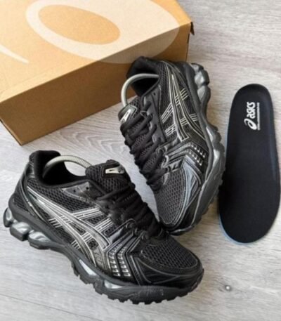 A pair of black and silver ASICS running shoes with a box and insoles on a light grey wooden floor, perfect for athletes seeking comfort and style.