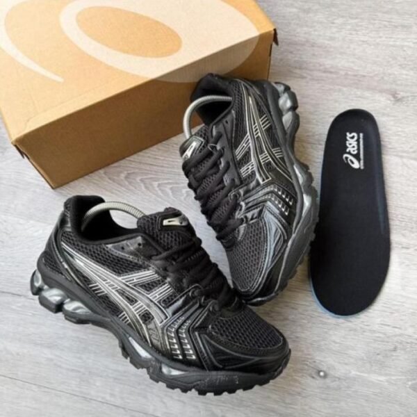 A pair of black and silver ASICS running shoes with a box and insoles on a light grey wooden floor, perfect for athletes seeking comfort and style.