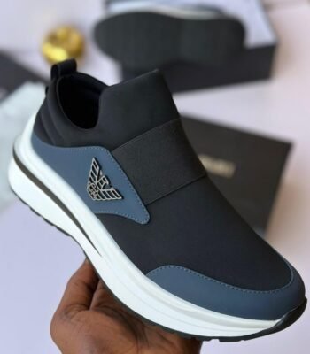 A close-up shot of a hand holding a black sneaker with a white sole and elasticated strap, showcasing the shoe's sleek design and luxurious details.
