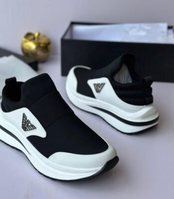 A pair of black and white Versace sneakers with logo detailing, displayed with a shoe box and accessories on a light grey background.