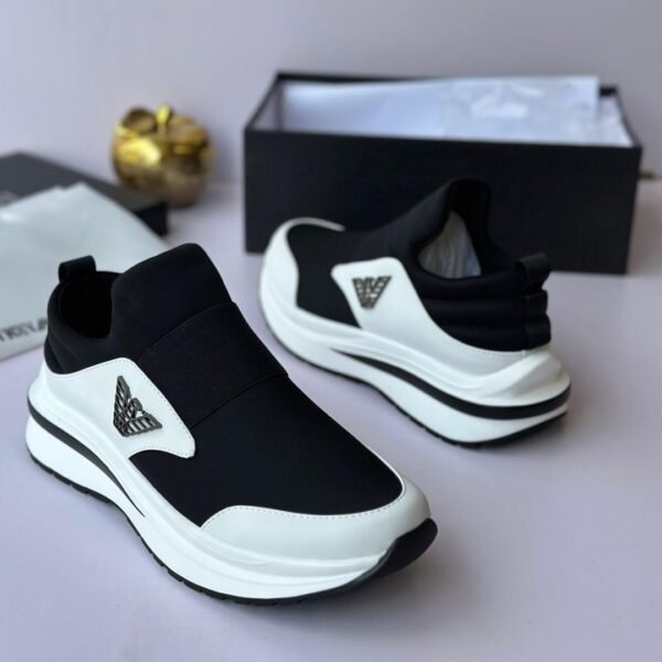 A pair of black and white Versace sneakers with logo detailing, displayed with a shoe box and accessories on a light grey background.