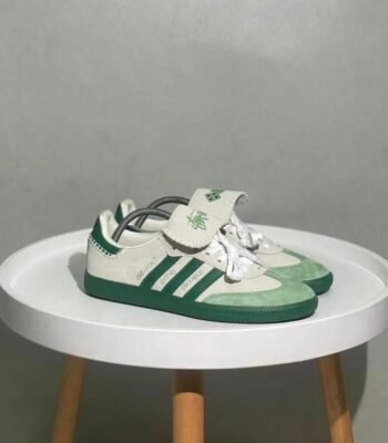 A pair of green and white Adidas Superstar sneakers on a white table, showcasing the shoe's sleek design and luxurious details.
