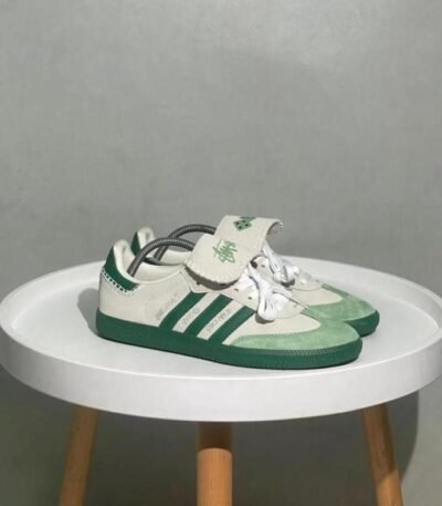 A pair of green and white Adidas Superstar sneakers on a white table, showcasing the shoe's sleek design and luxurious details.