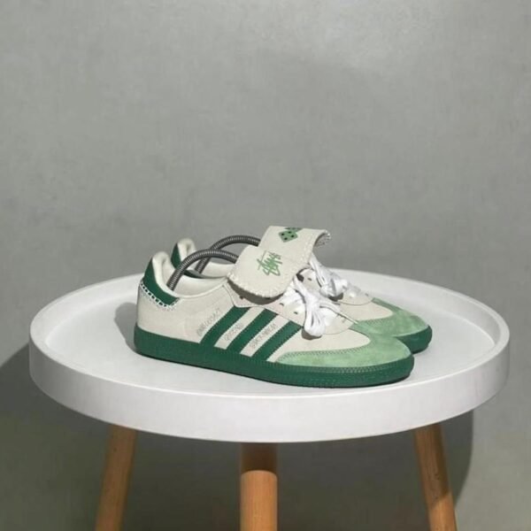 A pair of green and white Adidas Superstar sneakers on a white table, showcasing the shoe's sleek design and luxurious details.
