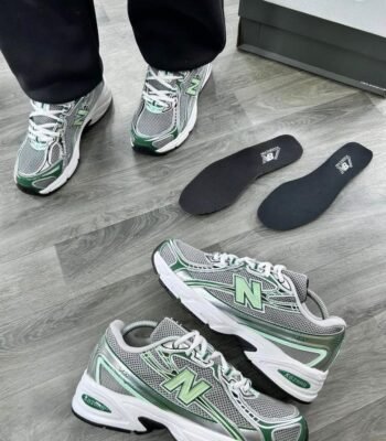 A pair of grey and green New Balance 574 sneakers on a wooden floor, showcasing the shoe's sleek design and Modern Luxury appeal.