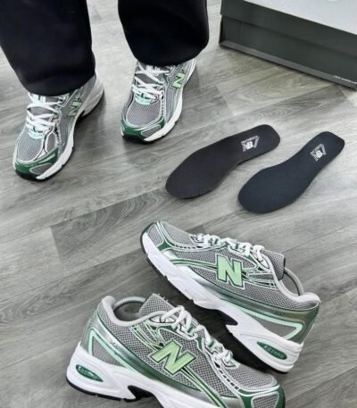 A pair of grey and green New Balance 574 sneakers on a wooden floor, showcasing the shoe's sleek design and Modern Luxury appeal.