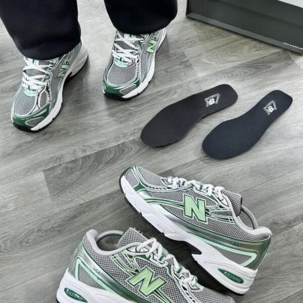 A pair of grey and green New Balance 574 sneakers on a wooden floor, showcasing the shoe's sleek design and Modern Luxury appeal.