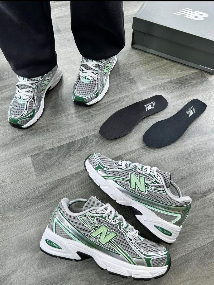 root A pair of grey and green New Balance 574 sneakers on a wooden floor, showcasing the shoe's sleek design and Modern Luxury appeal.