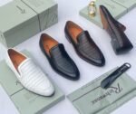 A pair of white leather loafers with perforated details, showcased on an open shoe box with elegant accessories, epitomizing luxury and sophistication.