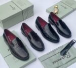 A pair of black crocodile pattern loafers with red interior, displayed on a shoe box with a luxurious background.