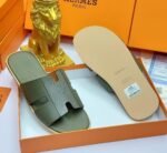 Black leather slide sandals in an orange box with a gold lion figurine, embodying modern luxury and timeless quality.
