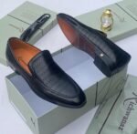 A pair of white leather loafers with perforated details, showcased on an open shoe box with elegant accessories, epitomizing luxury and sophistication.