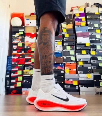 A close-up of a man's legs wearing white and red Nike ZoomX running shoes, showcasing the shoe's sleek design and vibrant colors.