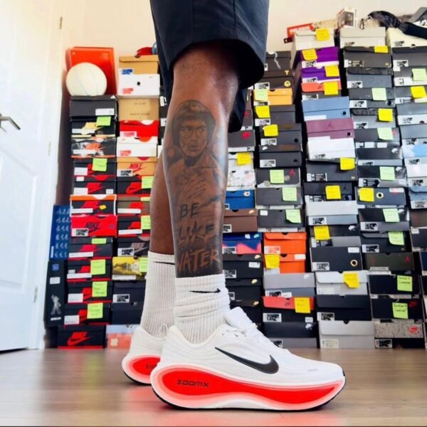 A close-up of a man's legs wearing white and red Nike ZoomX running shoes, showcasing the shoe's sleek design and vibrant colors.