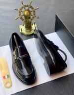 A pair of black patent leather loafers on a white paper with a shoe tree and a decorative ship's wheel in the background, embodying Modern Luxury and Urban Edge.