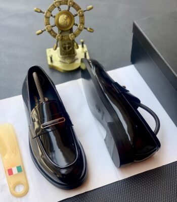 A pair of black patent leather loafers on a white paper with a shoe tree and a decorative ship's wheel in the background, embodying Modern Luxury and Urban Edge.