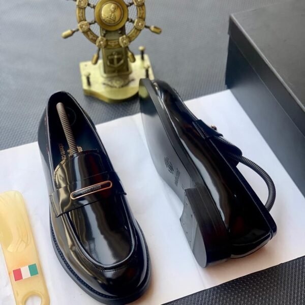 A pair of black patent leather loafers on a white paper with a shoe tree and a decorative ship's wheel in the background, embodying Modern Luxury and Urban Edge.