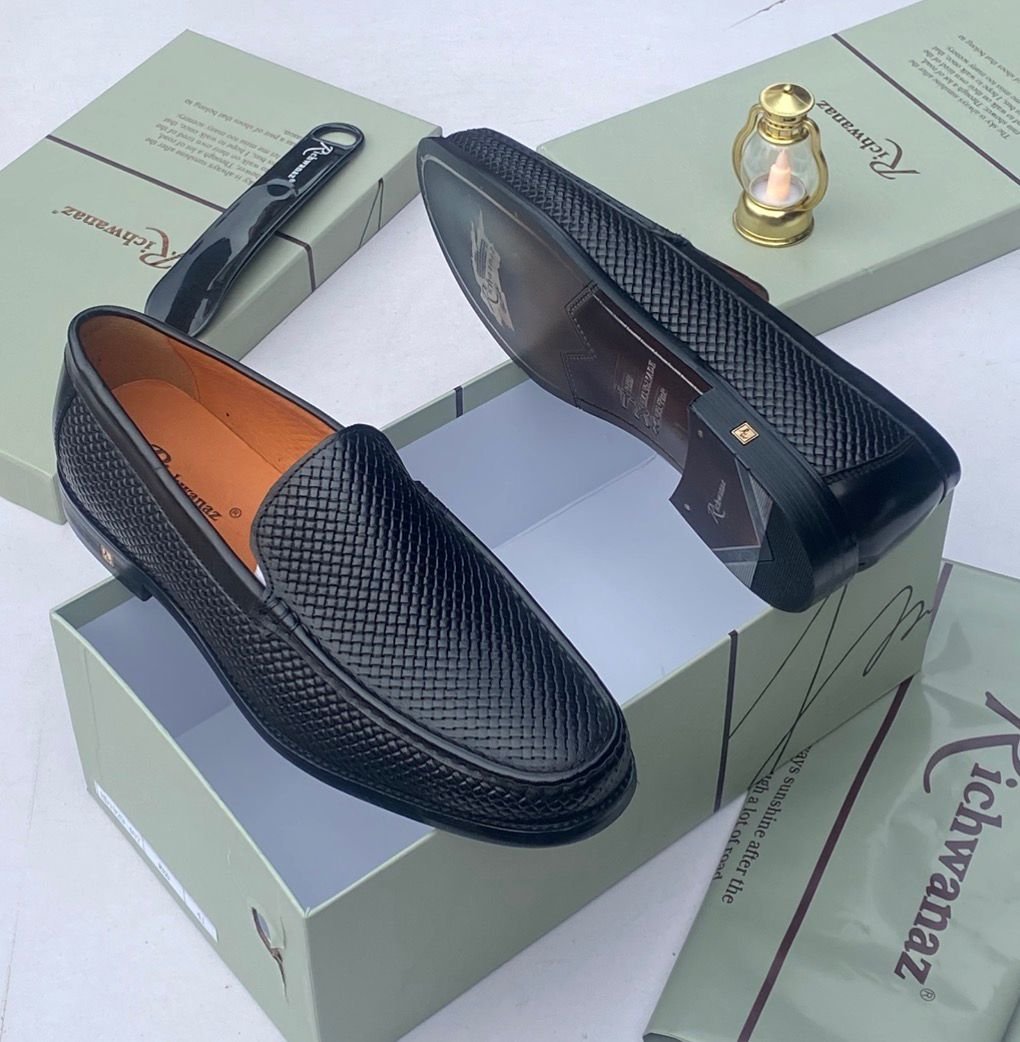 root A pair of black woven leather loafers displayed on a shoe box, showcasing the intricate details and craftsmanship of the shoes.