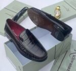 A pair of black crocodile pattern loafers with red interior, displayed on a shoe box with a luxurious background.