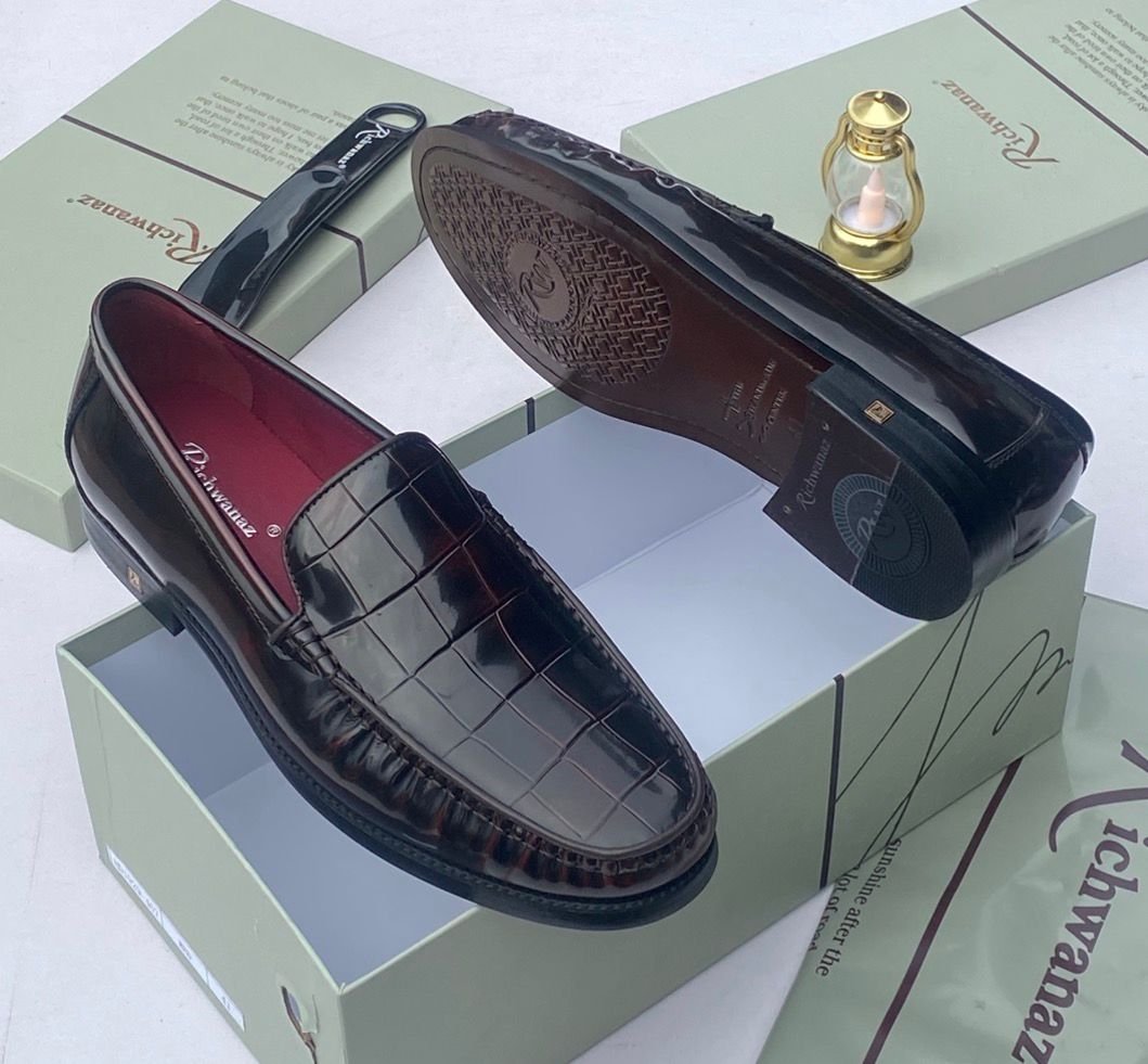 root A pair of black crocodile pattern loafers with red interior, displayed on a shoe box with a luxurious background.