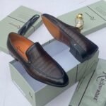 A pair of white leather loafers with perforated details, showcased on an open shoe box with elegant accessories, epitomizing luxury and sophistication.