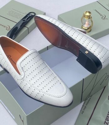 A pair of white leather loafers with perforated details, showcased on an open shoe box with elegant accessories, epitomizing luxury and sophistication.