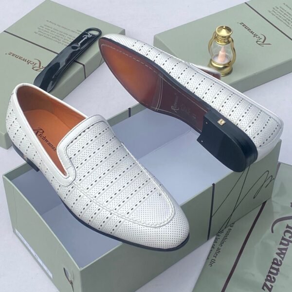 A pair of white leather loafers with perforated details, showcased on an open shoe box with elegant accessories, epitomizing luxury and sophistication.