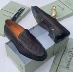 A pair of black woven leather loafers displayed on a shoe box, showcasing the intricate details and craftsmanship of the shoes.