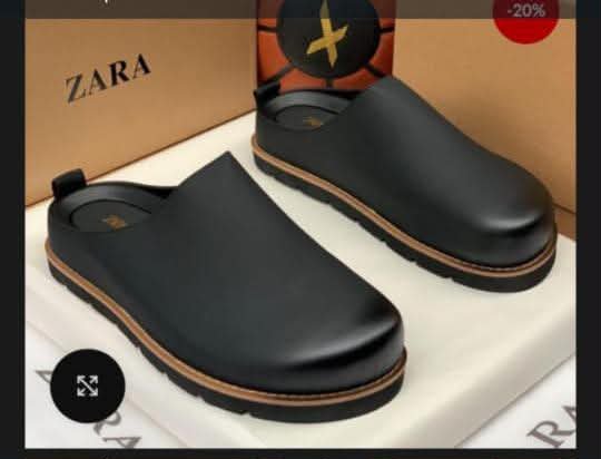 A pair of black leather clog shoes with a brown sole, presented on a white box with a Zara box in the background, showcasing modern luxury and urban edge.