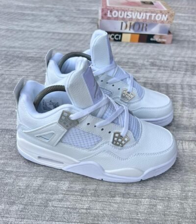A pair of white leather sneakers with diamond accents, placed on a wooden surface with luxury brand boxes in the background.