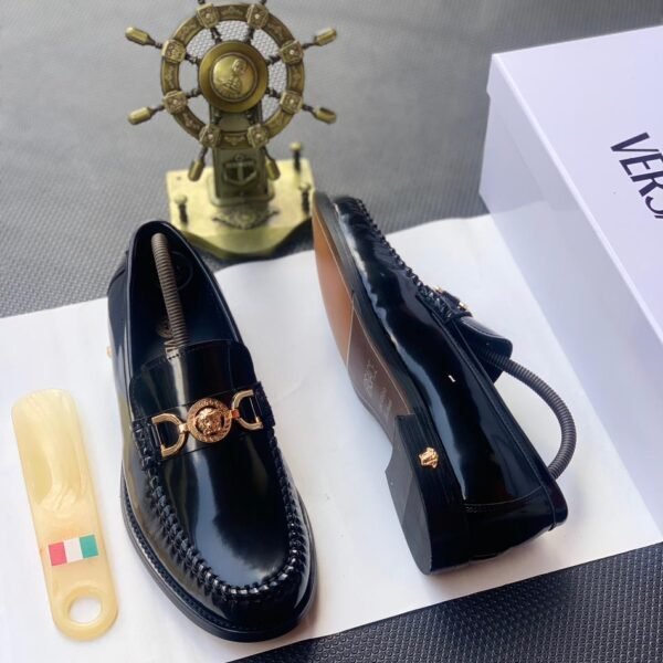 A pair of black leather loafers with a gold-tone Medusa buckle, presented on a white box with a shoe horn and a decorative ship's wheel in the background, embodying Modern Luxury and Urban Edge in Nigeria.