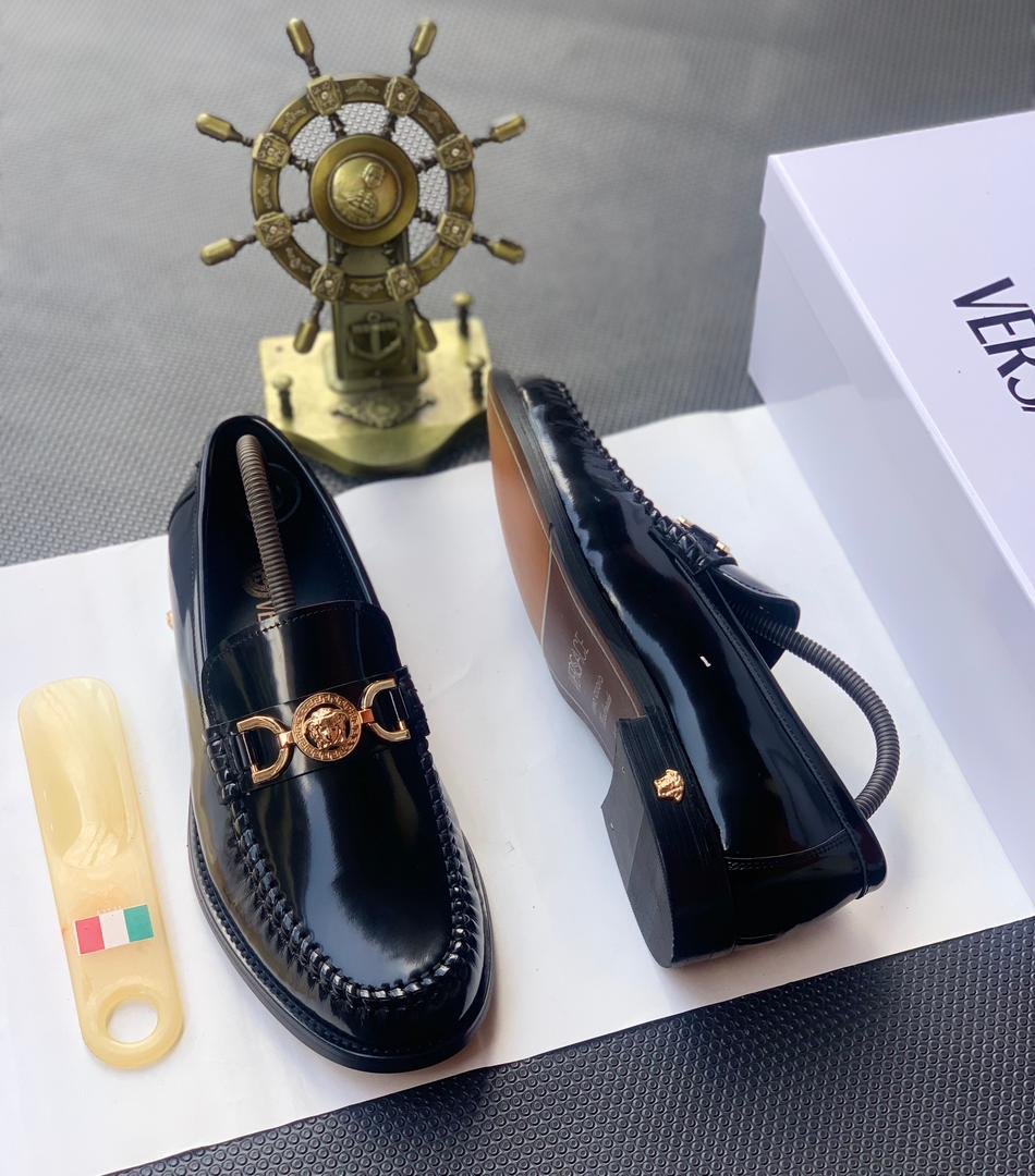 root A pair of black leather loafers with a gold-tone Medusa buckle, presented on a white box with a shoe horn and a decorative ship's wheel in the background, embodying Modern Luxury and Urban Edge in Nigeria.