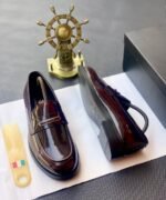 A pair of black patent leather loafers on a white paper with a shoe tree and a decorative ship's wheel in the background, embodying Modern Luxury and Urban Edge.