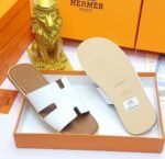 Black leather slide sandals in an orange box with a gold lion figurine, embodying modern luxury and timeless quality.