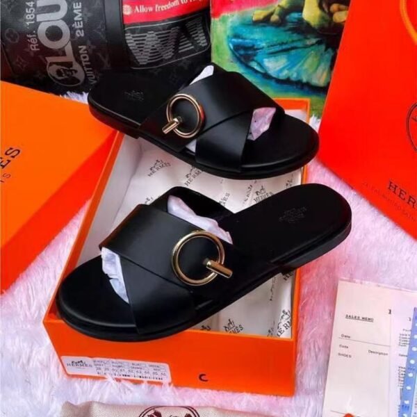 A pair of black leather slide sandals with a gold buckle, nestled in an orange box with luxury brand accessories, exuding modern luxury and urban sophistication.