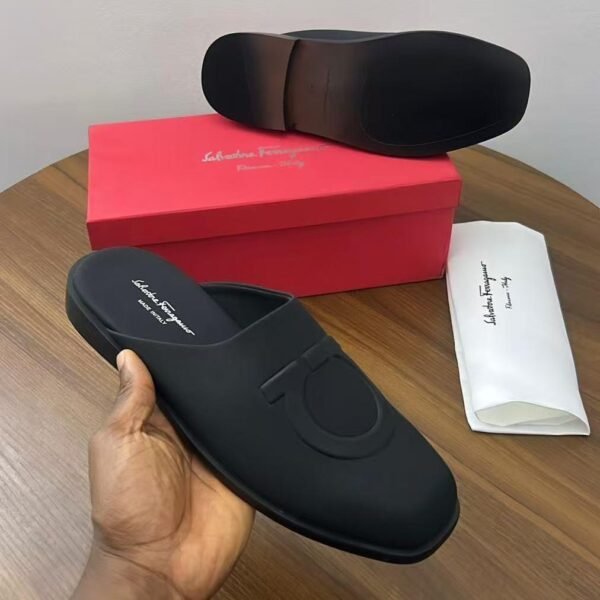 A pair of black leather mule loafers from Salvatore Ferragamo, displayed on a wooden table with the brand's signature red box and dust bag.