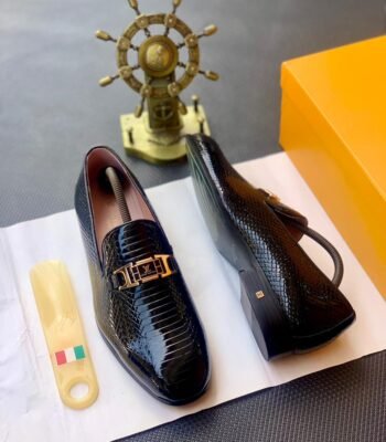 A pair of black leather loafers with a gold buckle on a white paper, showcasing Modern Luxury and Urban Edge design, with a hint of Timeless Quality in Nigeria.