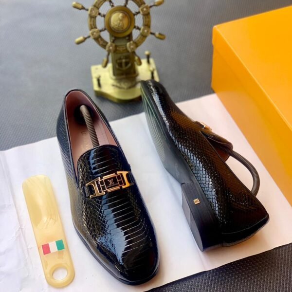 A pair of black leather loafers with a gold buckle on a white paper, showcasing Modern Luxury and Urban Edge design, with a hint of Timeless Quality in Nigeria.