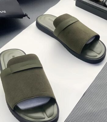 A pair of green ribbed slide sandals from Armani, displayed on a white surface with a black pouch and watch in the background, embodying Modern Luxury and Urban Edge.