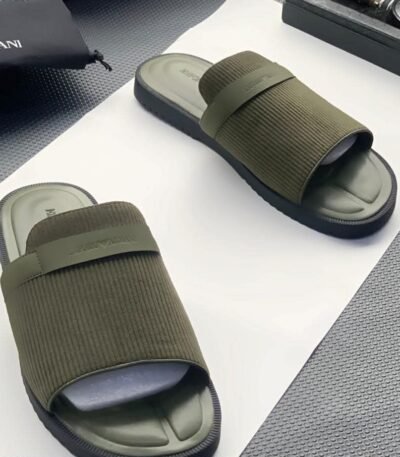 A pair of green ribbed slide sandals from Armani, displayed on a white surface with a black pouch and watch in the background, embodying Modern Luxury and Urban Edge.