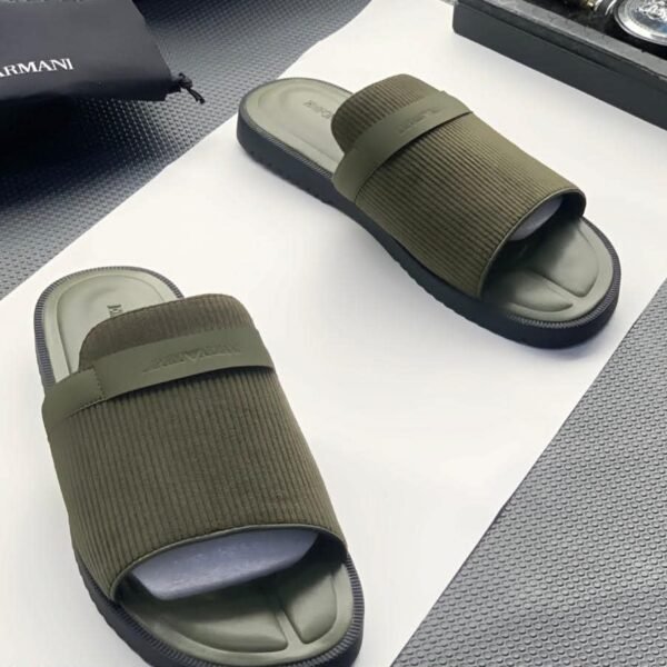 A pair of green ribbed slide sandals from Armani, displayed on a white surface with a black pouch and watch in the background, embodying Modern Luxury and Urban Edge.